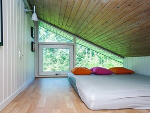 A bedroom with a sloped ceiling, a large window, and a bed with colorful pillows. - 4 Star Holiday Home in Bindslev (Bindslev)