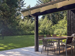 A covered outdoor patio with a table and chairs, surrounded by a grassy lawn and trees.