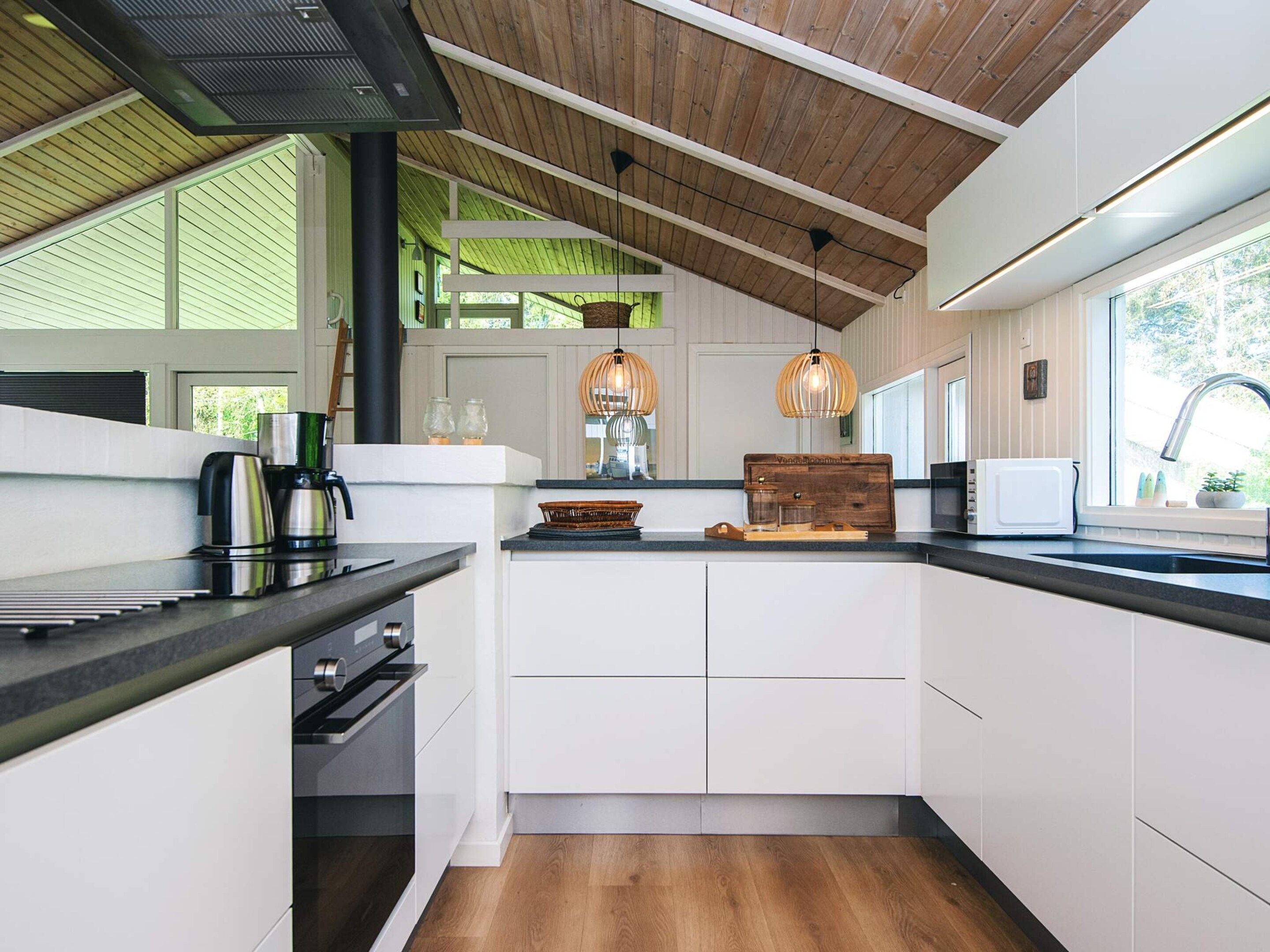 A modern kitchen with white cabinetry, a wooden ceiling, and pendant lighting.
