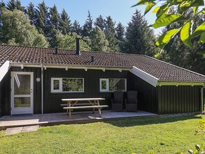 A wooden cabin with a tiled roof, a front door, two windows, a picnic table, and a small deck. - 4 Star Holiday Home in Bindslev (Bindslev)
