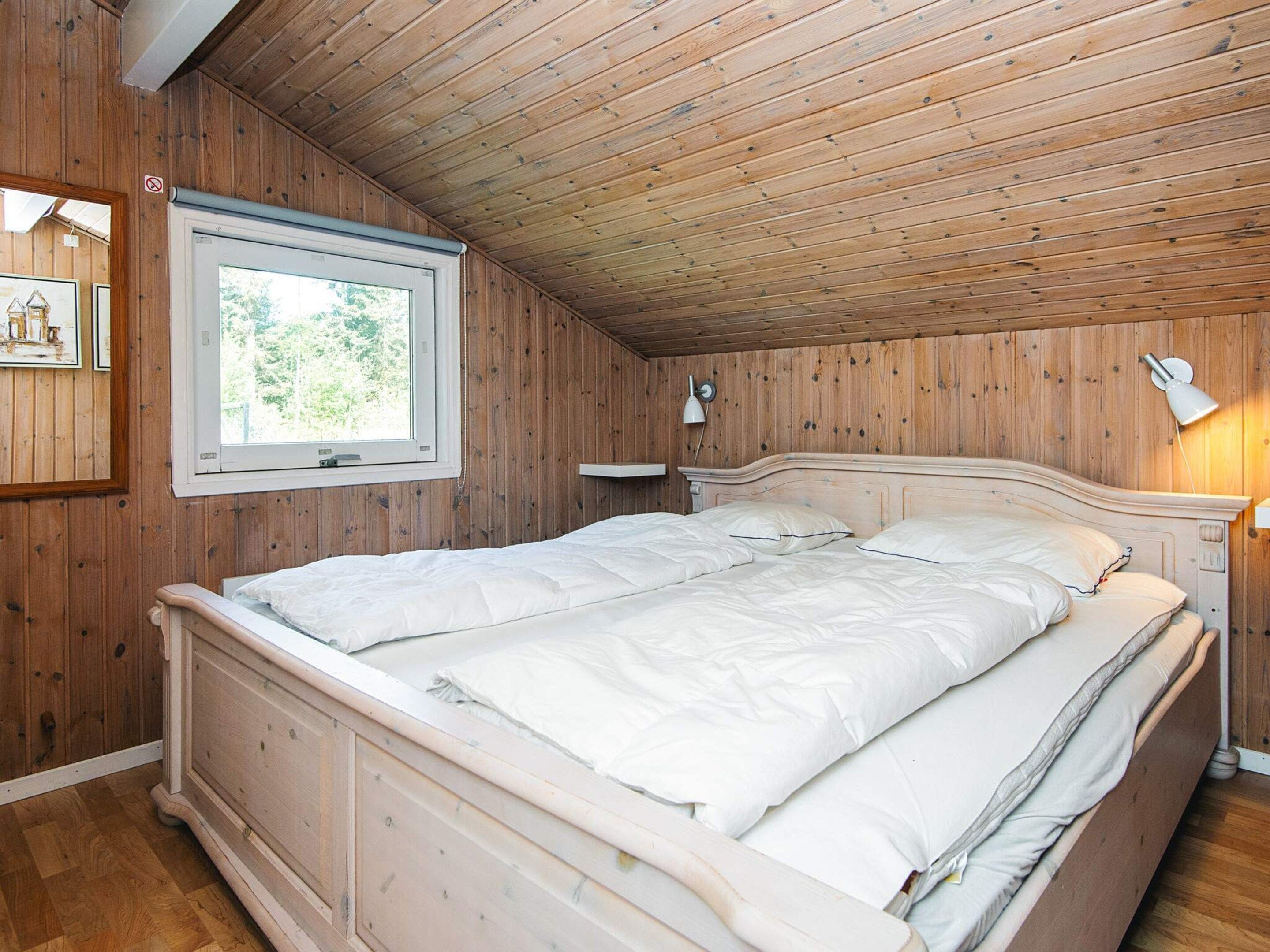 A wooden-paneled bedroom with a bed, a window, a wall-mounted lamp, and a framed picture.