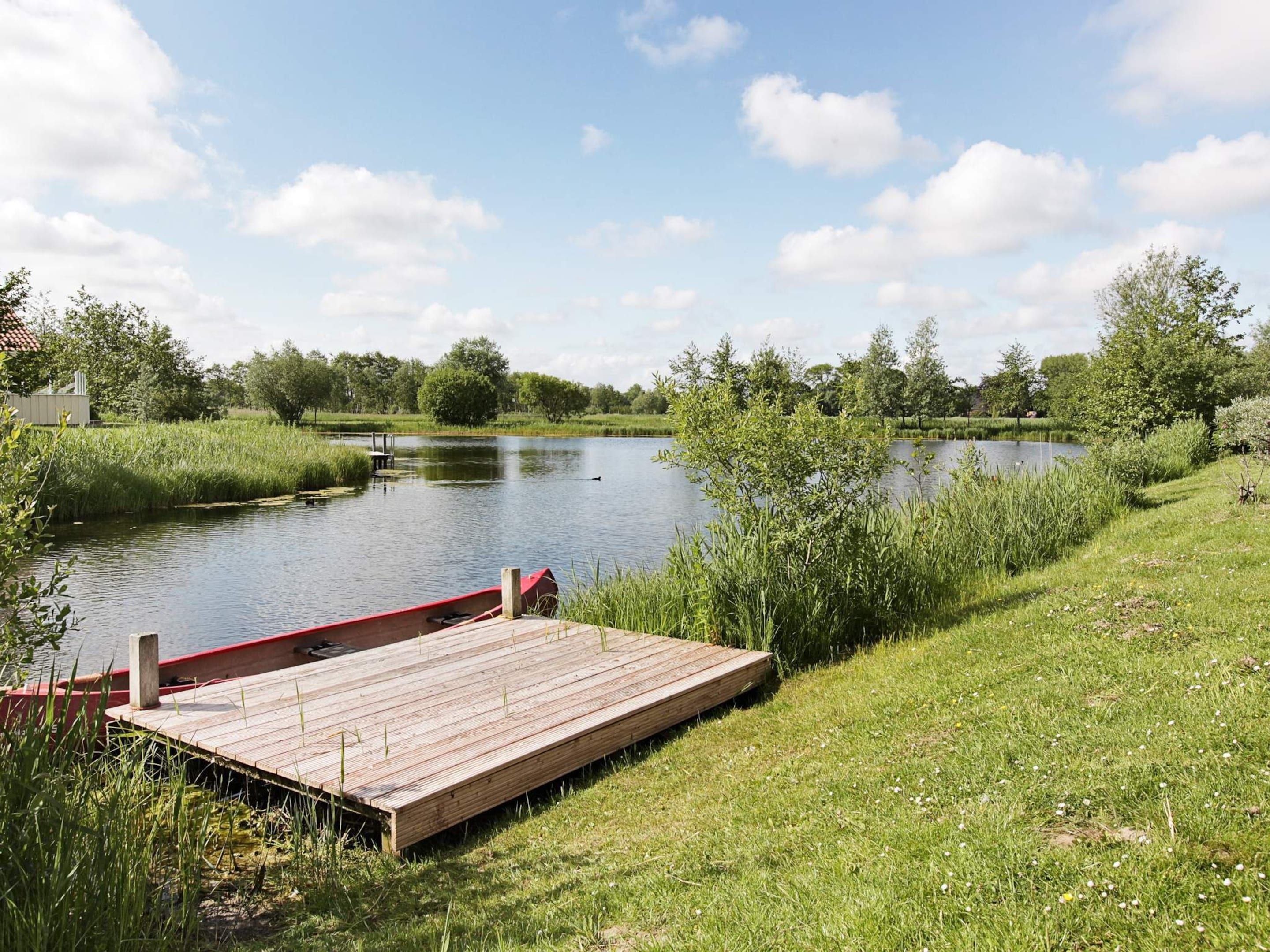 A wooden dock extending into a calm river surrounded by lush greenery and trees.