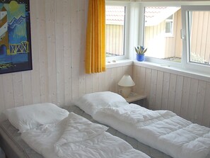 A room with two single beds, a window with a view of a building, and a painting on the wall.