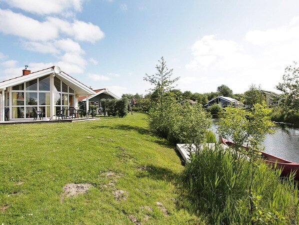 A lakeside property with a large glass conservatory, a grassy lawn, and a dock.