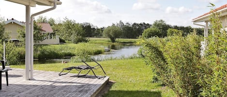 A wooden deck with a white pergola, a pond, and surrounding greenery.