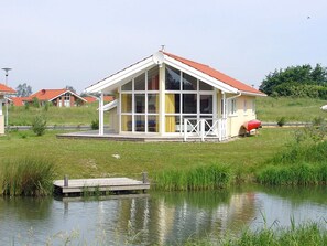 En envåningsbyggnad med ett rött tak och stora fönster, belägen intill en vattenyta med en brygga.