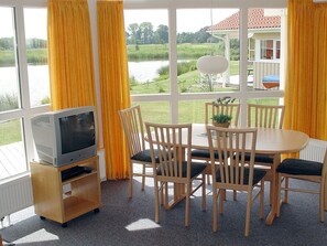 A dining area with a table and chairs, a television on a stand, and a view of a lake through large windows.