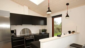 Cocina moderna con armarios negros, electrodomésticos de acero inoxidable, una isla central con taburetes e iluminación colgante.