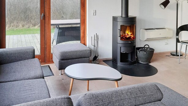 Una sala de estar moderna con una estufa de leña, sofás grises, una mesita y vistas al exterior a través de puertas de cristal.