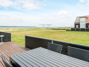 A deck with a table and chairs, overlooking a grassy area and a building with a red roof.