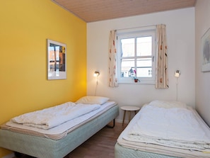 A room with two single beds, a small round table, a window with curtains, and a wall-mounted picture.