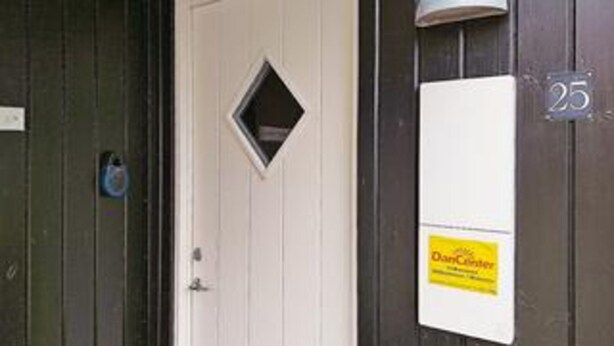 Uma porta com uma pequena janela, uma placa branca com texto amarelo e o número '25' na parede.