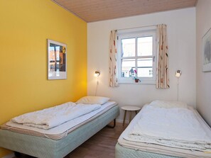 A room with two single beds, a small round table, a window with curtains, and a wall-mounted picture.