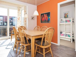 A dining area with a wooden table and chairs, a painting on the wall, and a view through a glass door.