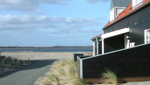 Um imóvel à beira-mar com vista para a praia, um deck de madeira e um edifício moderno com telhado vermelho.