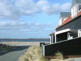 Una propiedad costera con vista a la playa, una terraza de madera y un edificio moderno con techo rojo.
