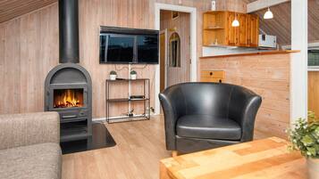 A cozy living room with a fireplace, wooden walls, a comfortable chair, and a dining table.