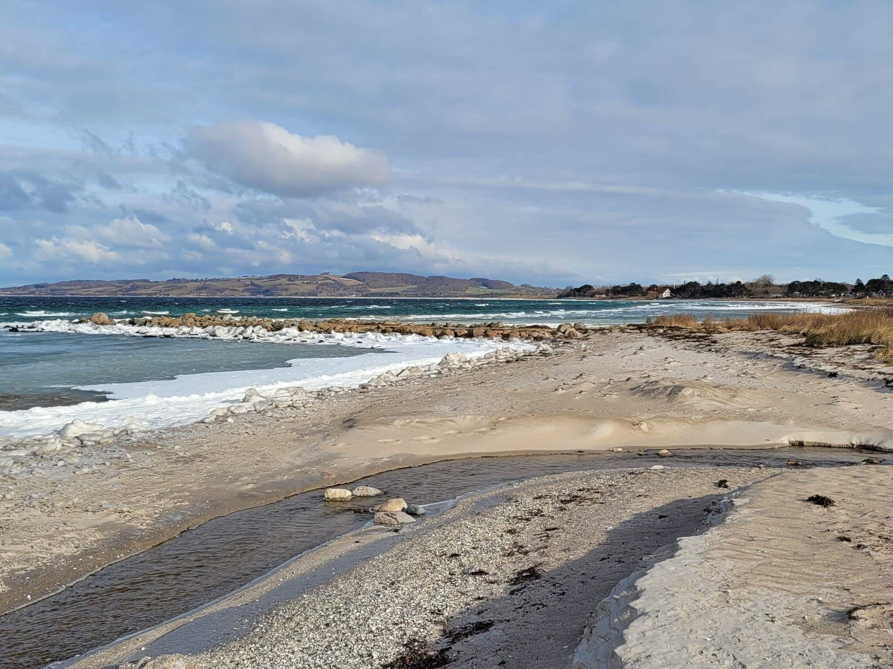 A coastal landscape with a rocky shoreline, waves, and distant hills.