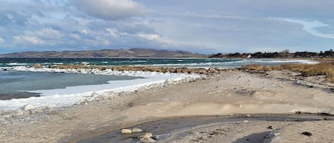 Paisagem costeira com linha de costa rochosa, ondas e colinas ao longe.
