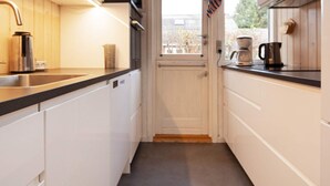 Una cocina estrecha con armarios blancos, una encimera negra y una ventana con vistas a árboles.