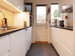 A narrow kitchen with white cabinets, a black countertop, and a window with a view of trees. - 6 Person Holiday Home in Vaeggerlose (Vaeggerlose)