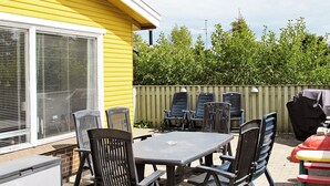 Un patio al aire libre con mesa y sillas, una parrilla y una casa amarilla al fondo.