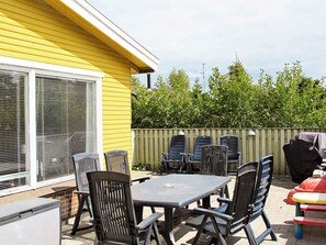 En uteplats med ett bord och stolar, en grill och ett gult hus i bakgrunden.