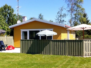 Ett gult hus med ett grönt staket, ett vitt parasoll och en röd bil på gården.