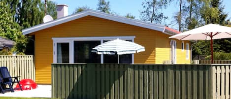 A yellow house with a green fence, a white umbrella, and a red car in the yard.