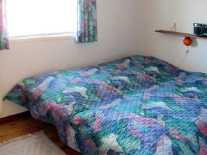 Un petit lit bien fait, avec une couverture colorée, un tapis blanc et une fenêtre avec des rideaux.