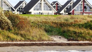 A row of beach houses with large windows and a boat on the shore. - Holiday Home in Wendtorf (Wendtorf)