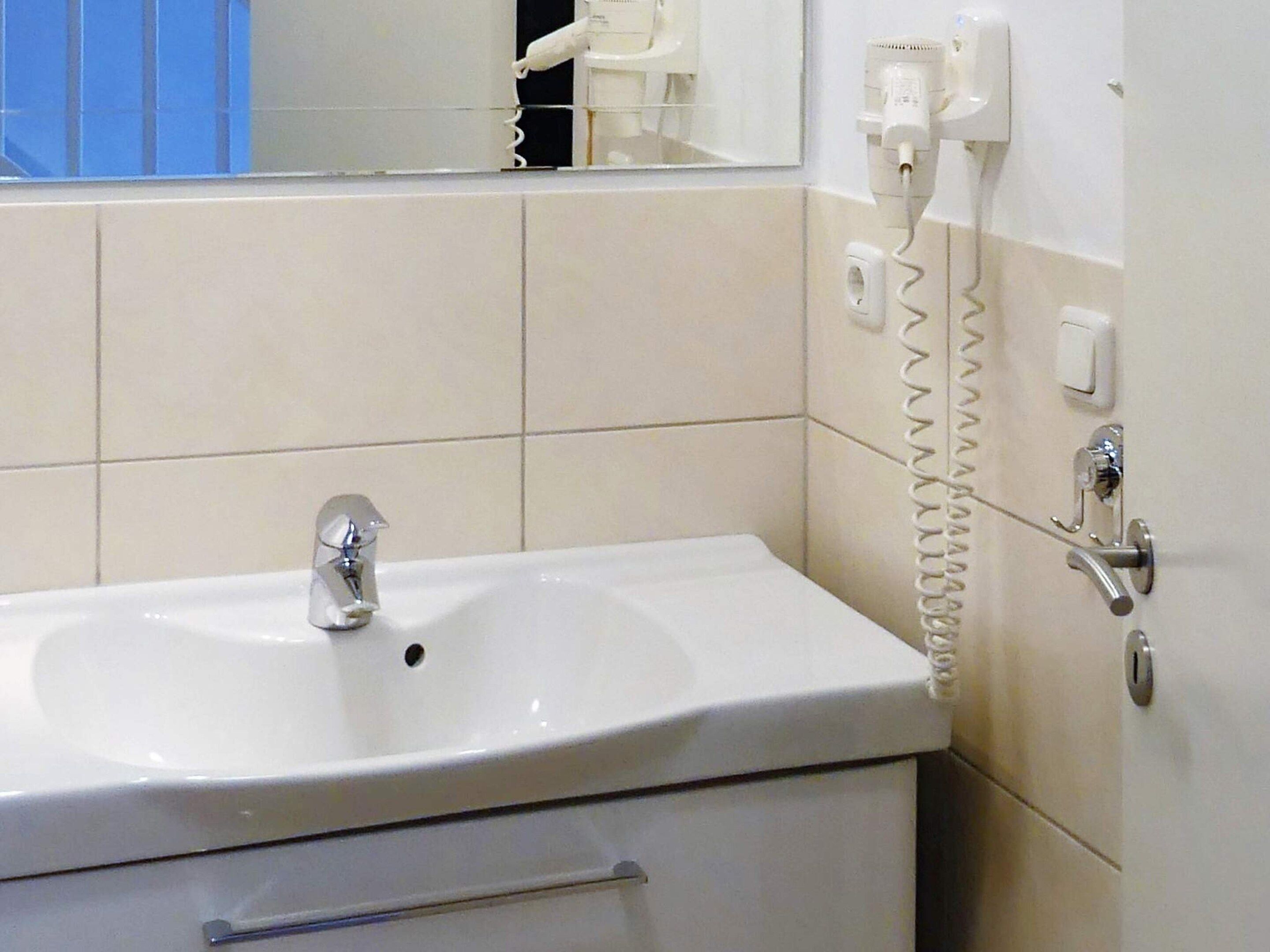 A bathroom with a white sink, a mirror, and a telephone mounted on the wall.