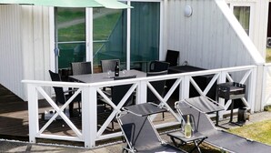 An outdoor patio with a table and chairs, a green umbrella, and lounge chairs. - Holiday Home in Wendtorf (Wendtorf)