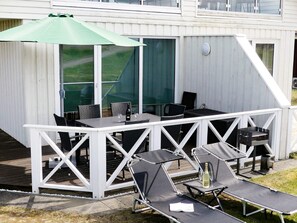 An outdoor patio with a table and chairs, a green umbrella, and lounge chairs. - Holiday Home in Wendtorf (Wendtorf)