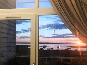 A room with a large window overlooking a body of water during sunset.