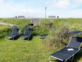 A grassy area with multiple sun loungers and benches, a lamp post, and a staircase leading to a higher elevation.