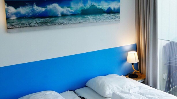 A hotel room with a bed, a nightstand with a lamp, and a painting of a wave on the wall. - Holiday Home in Wendtorf (Wendtorf)