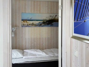A small, single-bed room with a wooden wall and a painting of a beach scene.