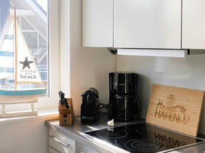 A kitchen with a coffee maker, a wooden cutting board with text, and a decorative sailboat by the window.