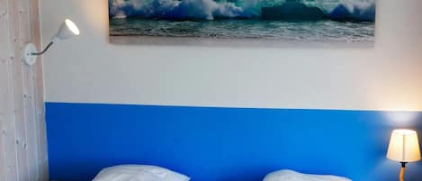 A hotel room with a bed, two bedside lamps, a wall-mounted painting of a wave, and a wooden nightstand.