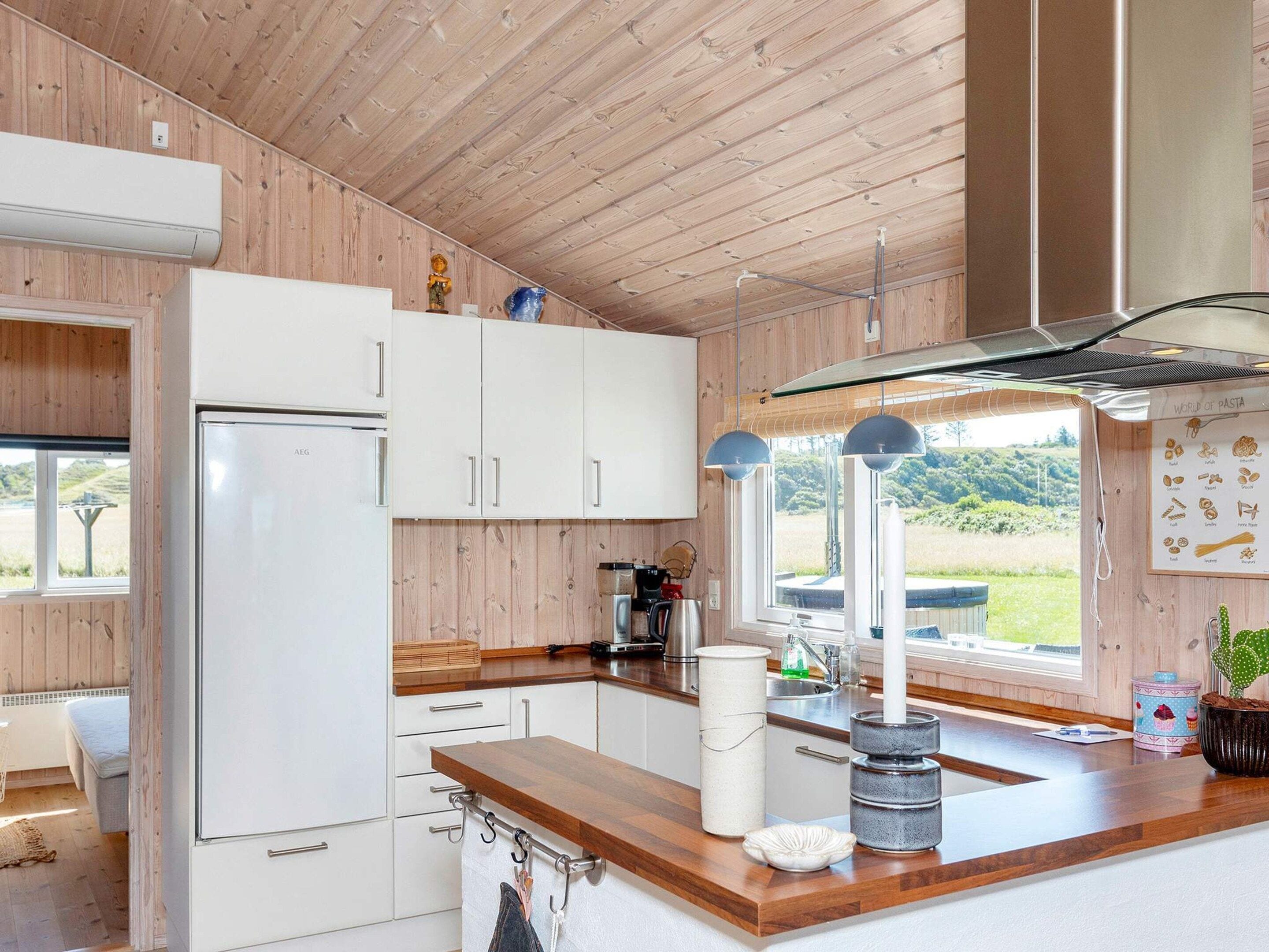 A modern kitchen with wooden walls, white cabinets, a wooden countertop, and a window with a view of greenery.