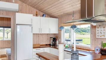 A modern kitchen with wooden walls, white cabinets, a wooden countertop, and a window with a view of greenery.