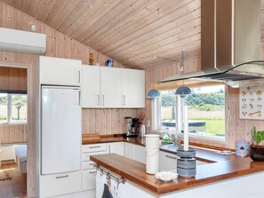 A modern kitchen with wooden walls, white cabinets, a wooden countertop, and a window with a view of greenery. - 5 Star Holiday Home in Hjorring (Hjørring)