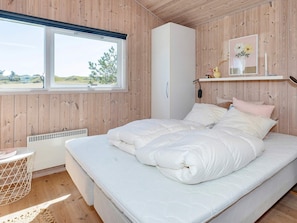 A bedroom with a bed, a window, a white wardrobe, and a shelf with decorative items.