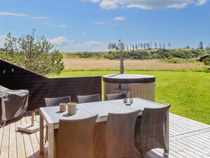 A wooden deck with a table and chairs, a hot tub, and a view of a grassy field and trees. - 5 Star Holiday Home in Hjorring (Hjørring)
