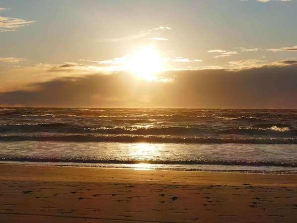 A beach with waves and a sun setting or rising in the background.