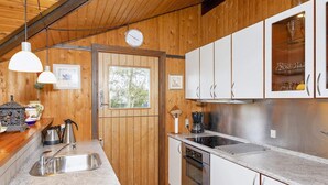 A compact kitchen with wooden walls, a stainless steel sink, a stove, and white cabinets. - 6 Person Holiday Home in Vestervig (Vestervig)