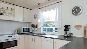A modern kitchen with white cabinets, a black countertop, a microwave, a stove, a sink, and a coffee maker. - 6 Person Holiday Home in Allingabro-by Traum (Allingåbro)