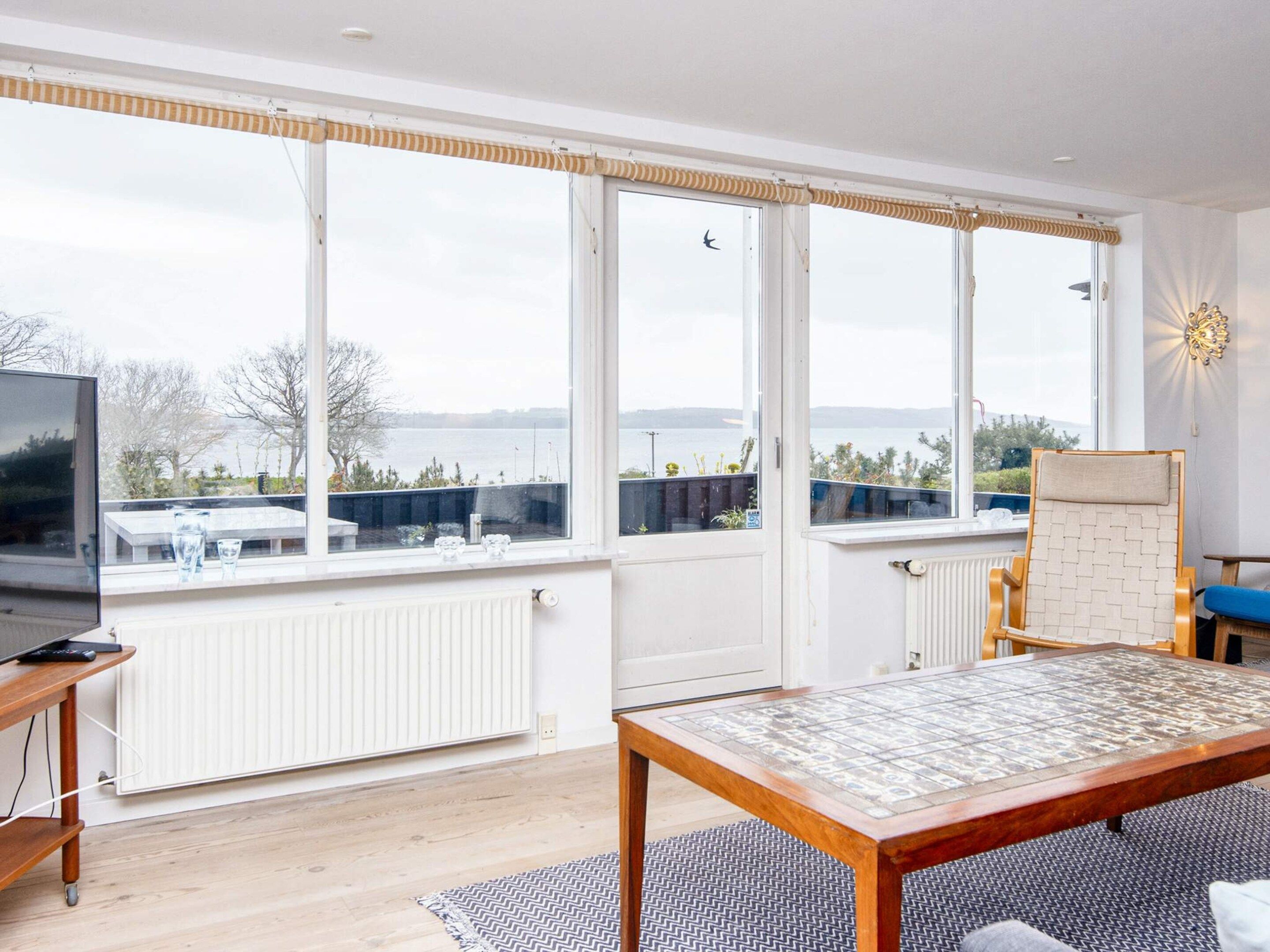 Una habitación amplia con ventanas grandes, una mesa de madera, una silla y un televisor sobre un mueble.