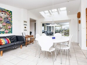 A modern living room with a black sofa, white chairs, a dining table, and a large window. - 6 Person Holiday Home in Borkop (Borkop)